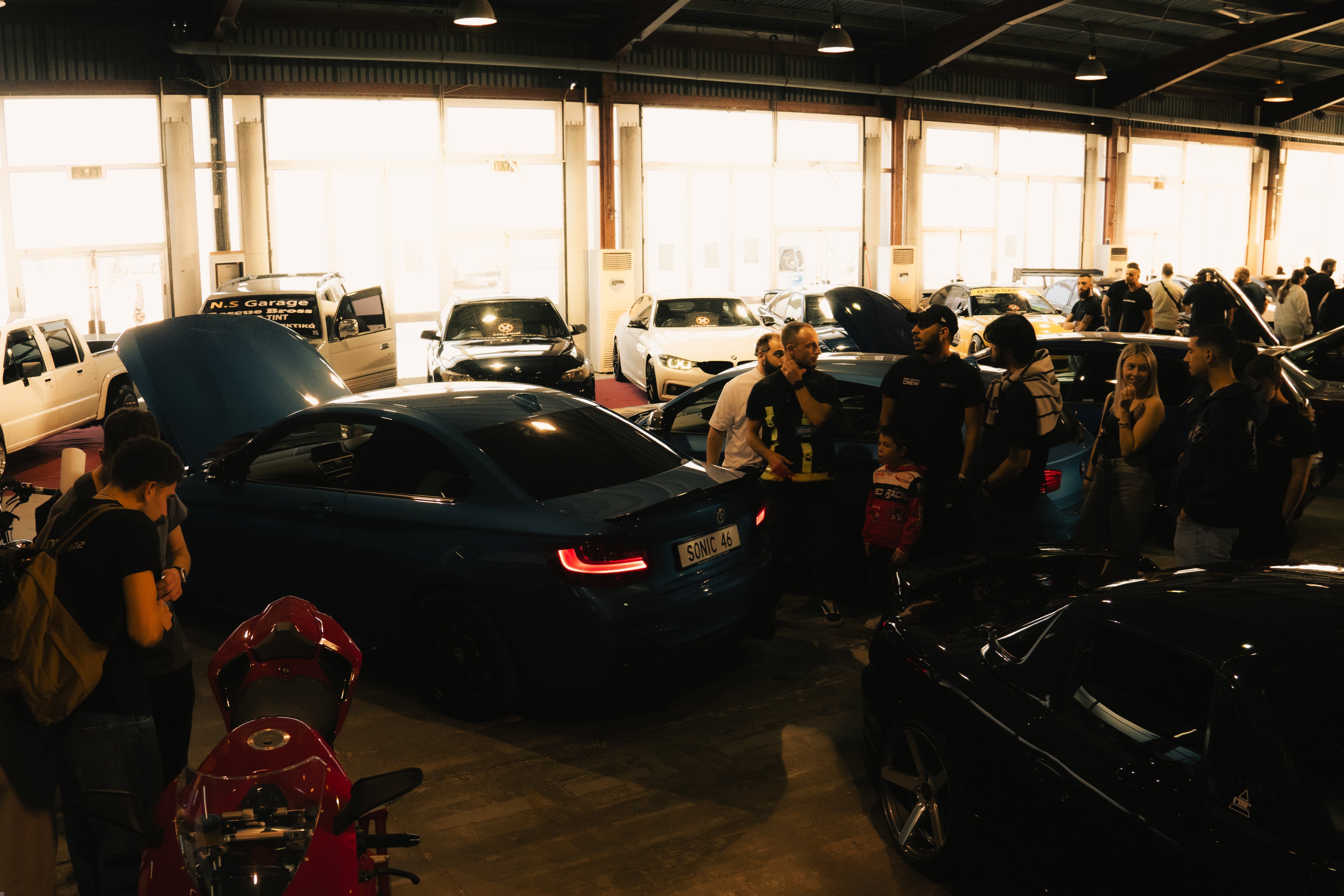 Car show or garage with multiple cars and people around them.