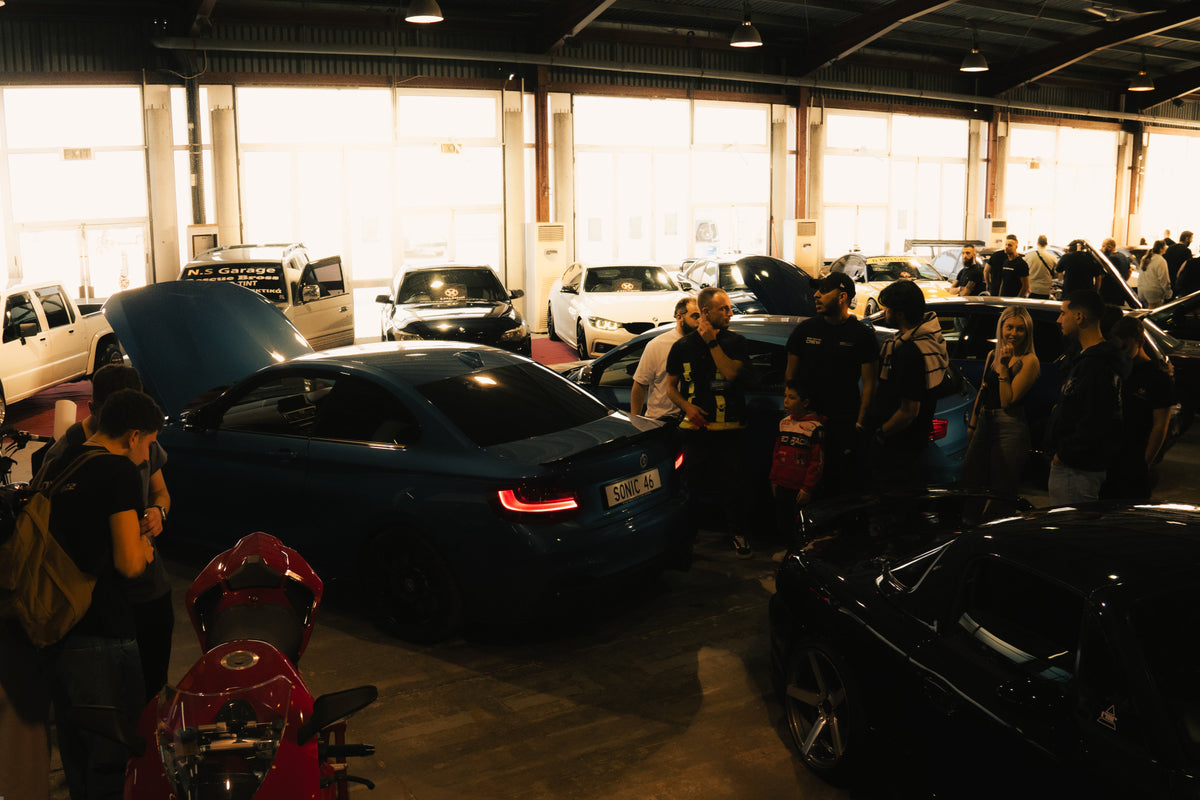 Car show or garage with multiple cars and people around them.