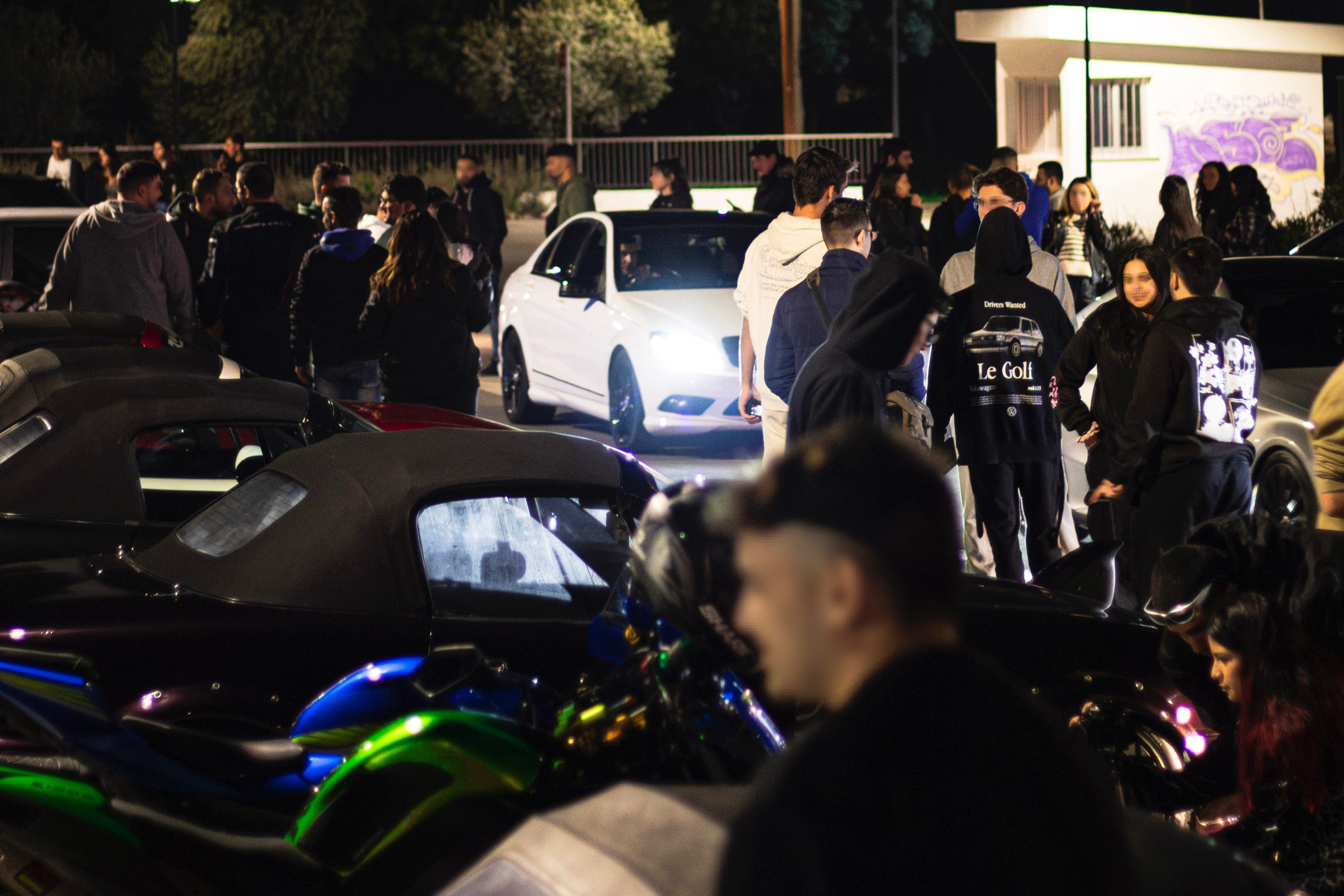 Group of people gathered around a white car at night.